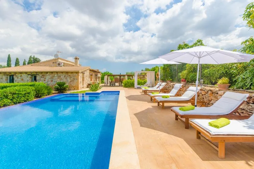 An outdoor pool beside a sunny lounging area with cushioned seating and umbrellas.