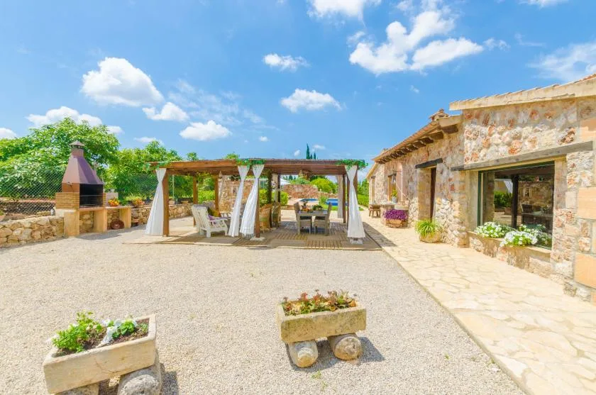 A stone courtyard features a shaded pergola dining area and a built-in outdoor grill.