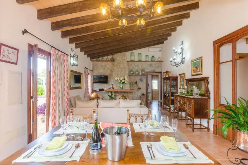 A dining area with a set table opens onto a living room beneath exposed wooden beams.