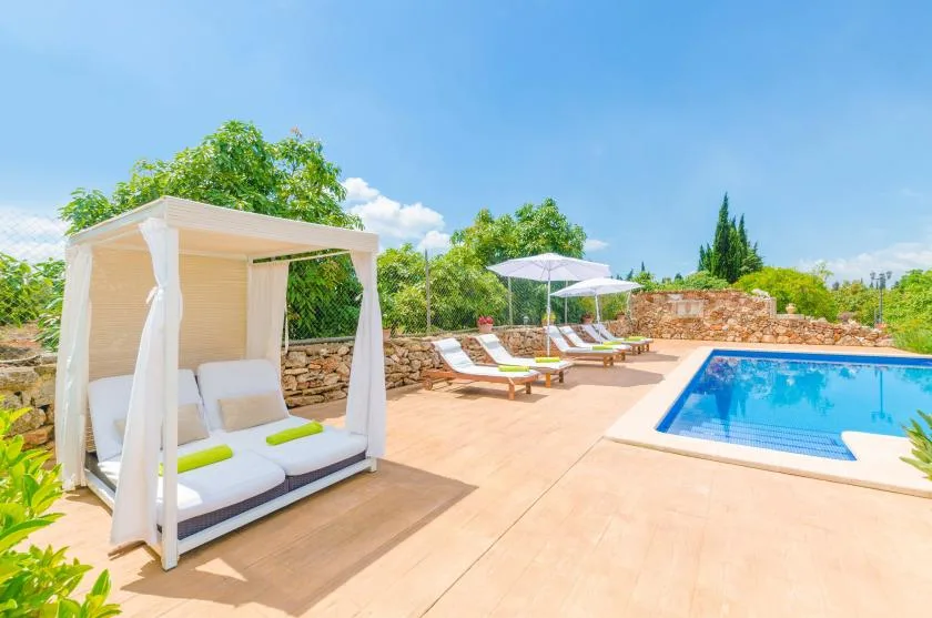 An outdoor pool beside a shaded daybed and sun loungers.
