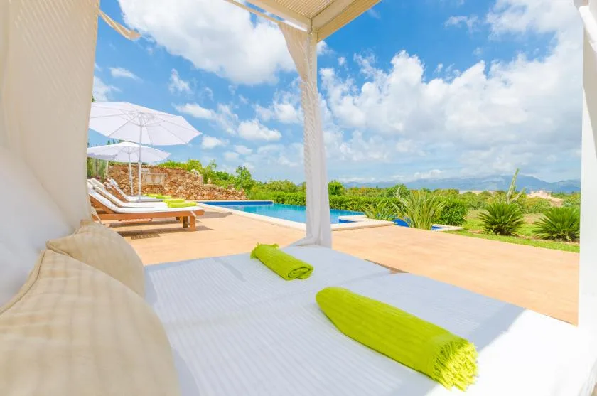 A covered outdoor lounge opens onto a pool, with sun loungers and green cushions.