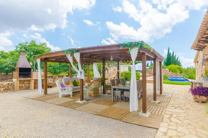 A shaded wooden pergola covers an outdoor seating area beside a stone-paved courtyard.