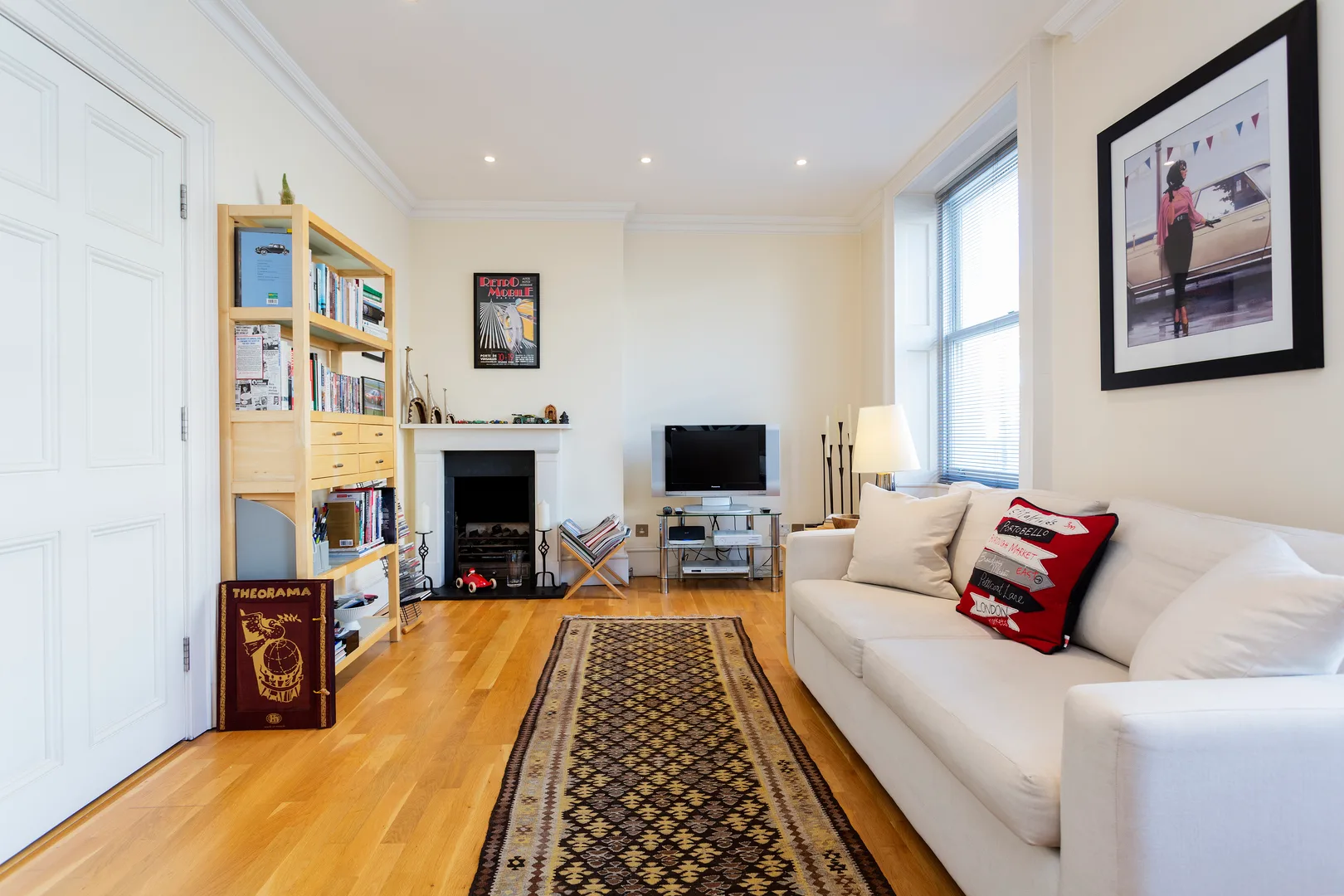 A bright living room with a white sofa, wooden floor, and patterned rug.