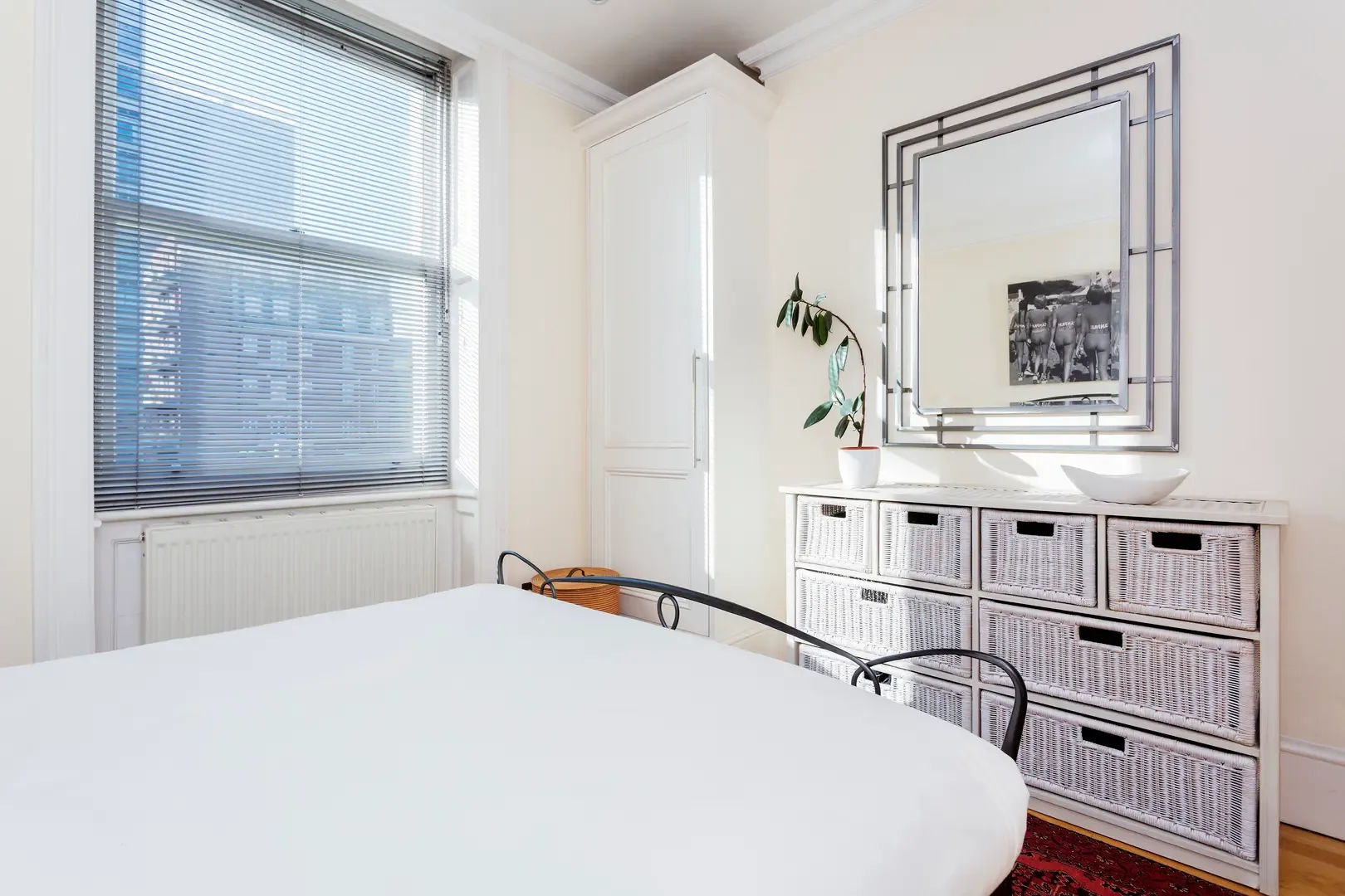 A bright bedroom with a bed, window, and white storage drawers.