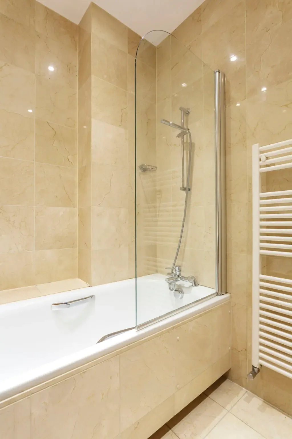 A bathtub with a glass shower screen sits in a tiled bathroom.