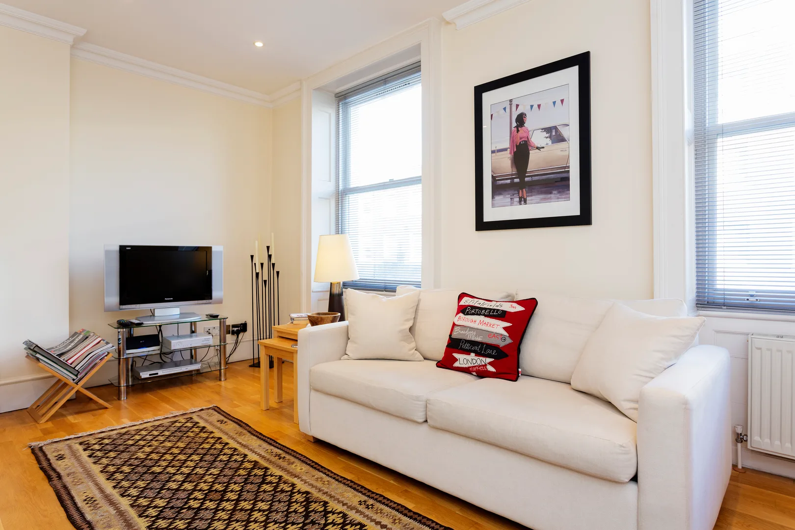 A bright living room with a white sofa and television beside tall windows.