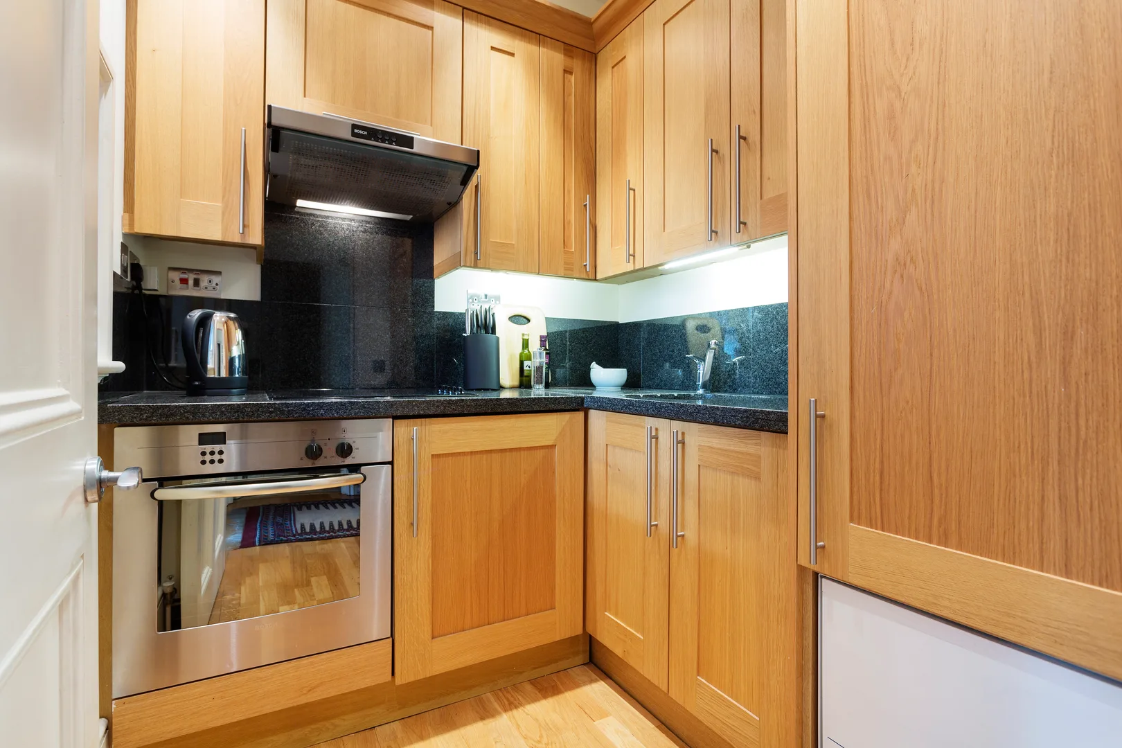 A compact kitchen with wooden cabinets, a built-in oven, and dark countertops.