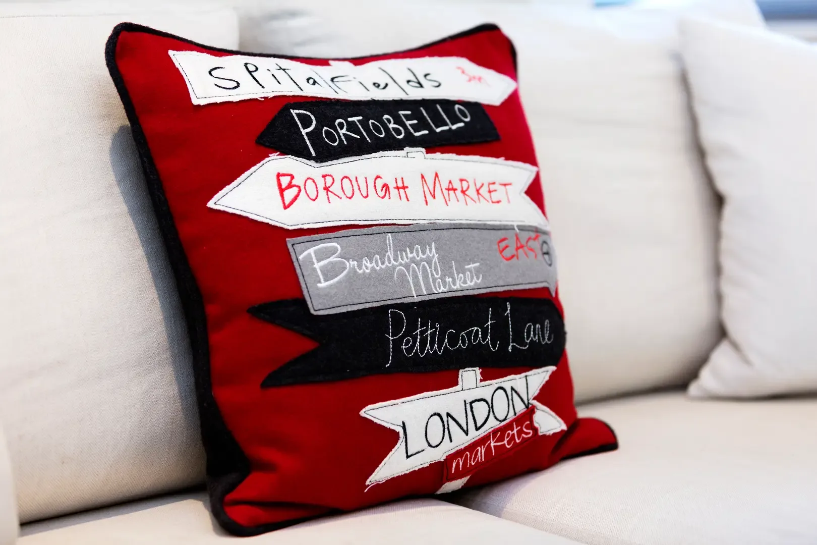 A red decorative cushion with embroidered names rests on a light-colored sofa.
