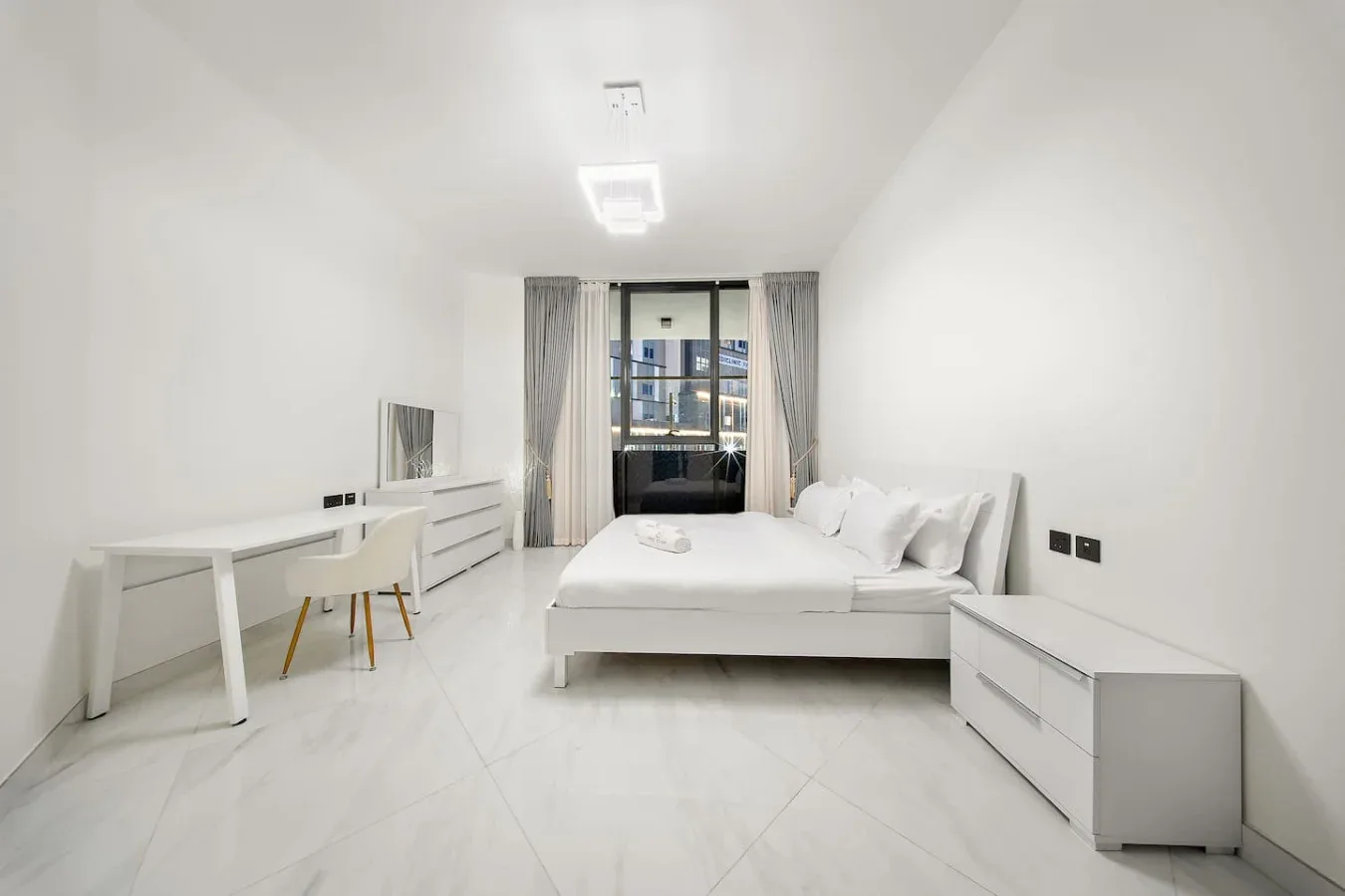 A bright bedroom with a bed, desk, and large window.