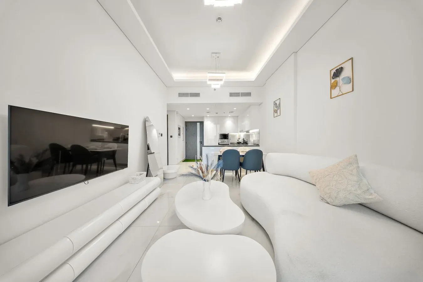 A bright living room with white seating, a television, and a dining area.