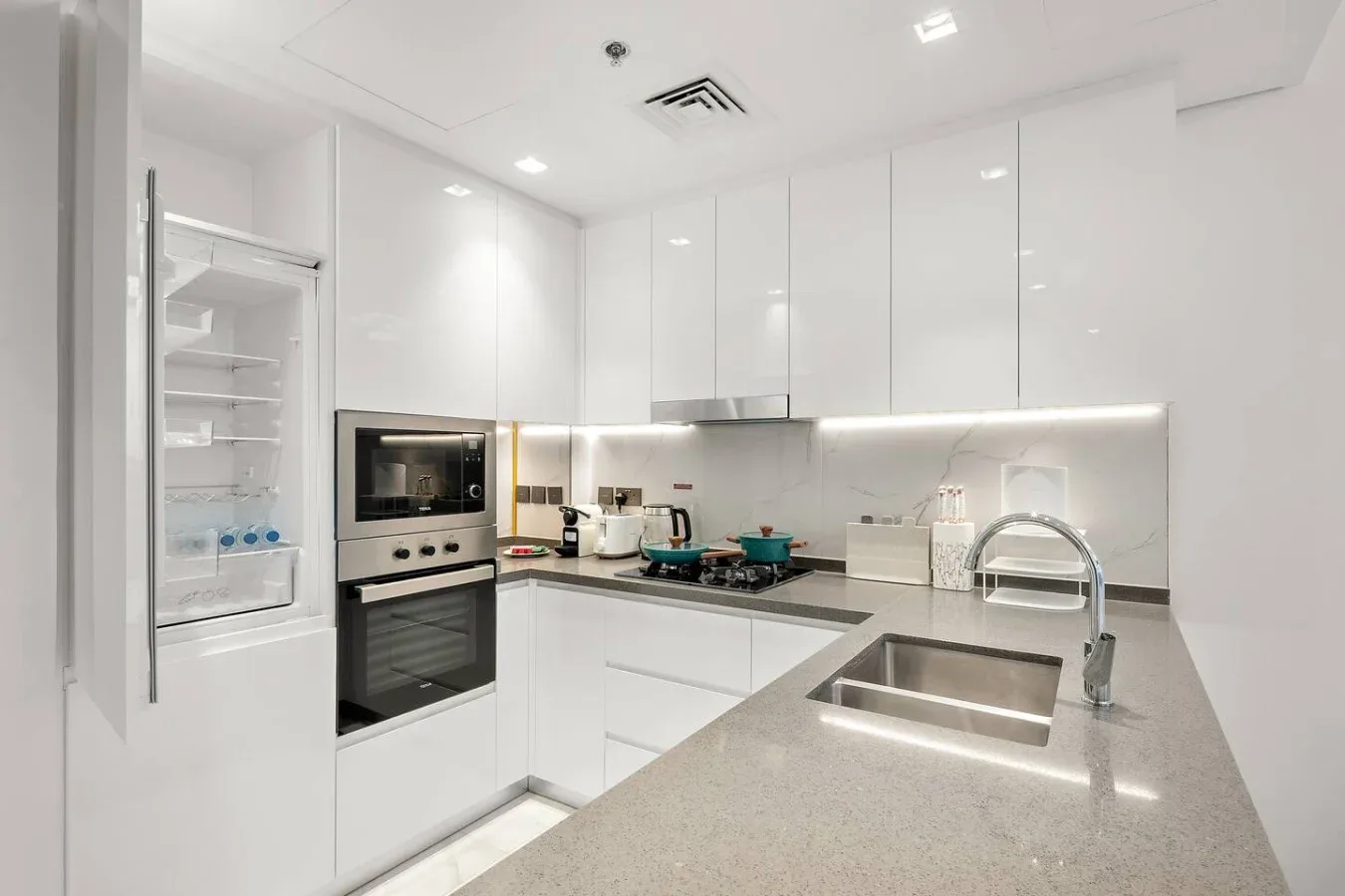 A modern white kitchen with built-in appliances and a broad countertop.