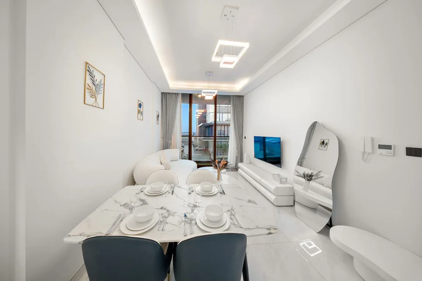 A bright dining and living area has a set dining table and a television.