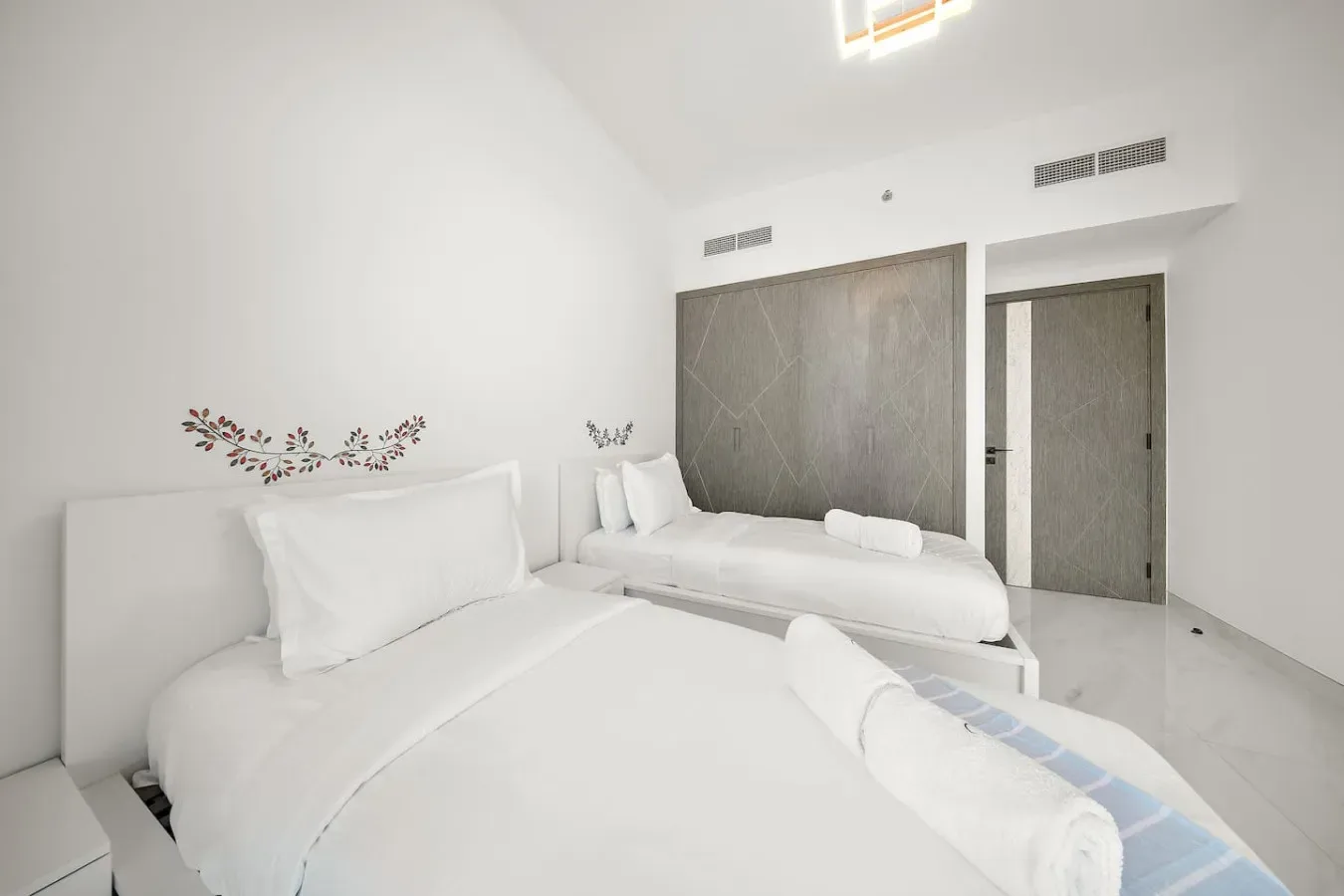 A bright bedroom with two beds and a dark accent wall.