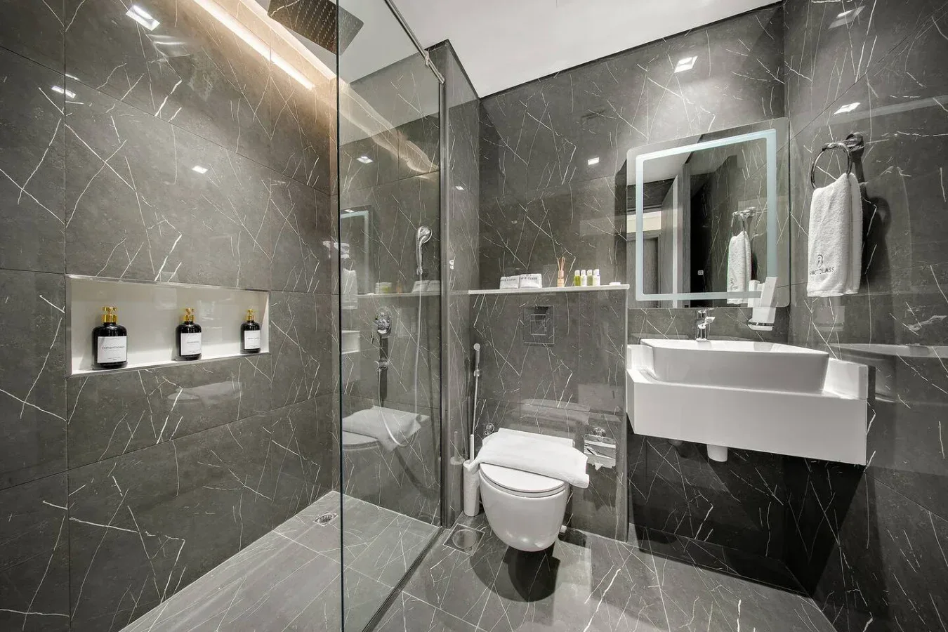 A modern bathroom with a glass shower, toilet, and wall-mounted sink.