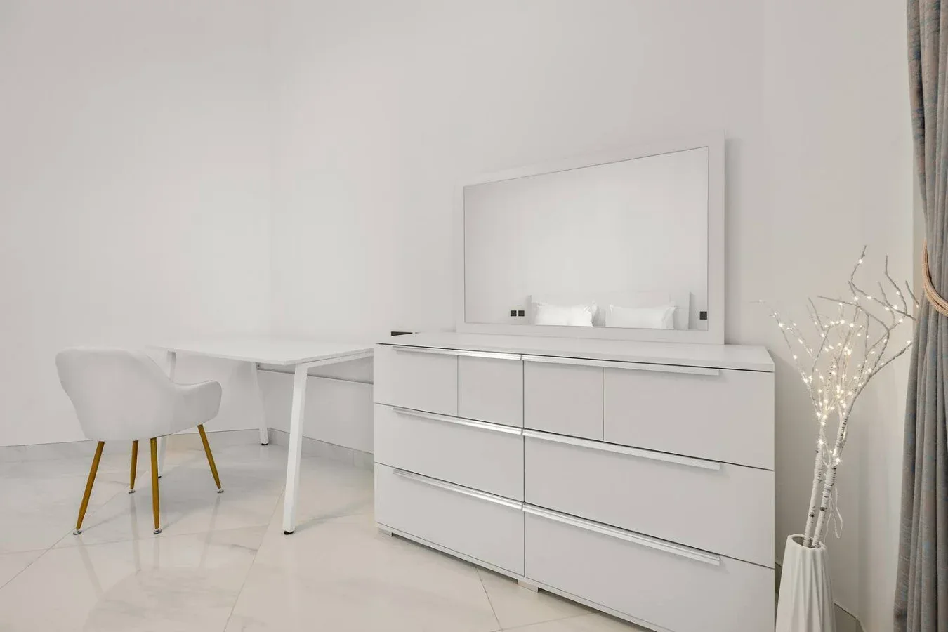 A bright bedroom dressing area with a large dresser, mirror, and desk.