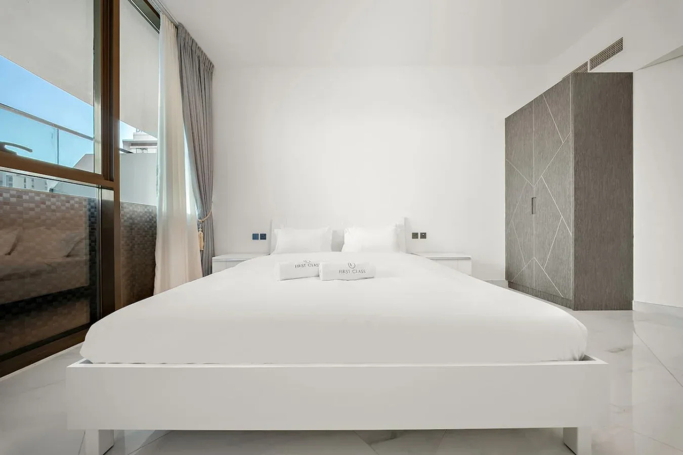 A bright bedroom with a white bed and a tall wardrobe.