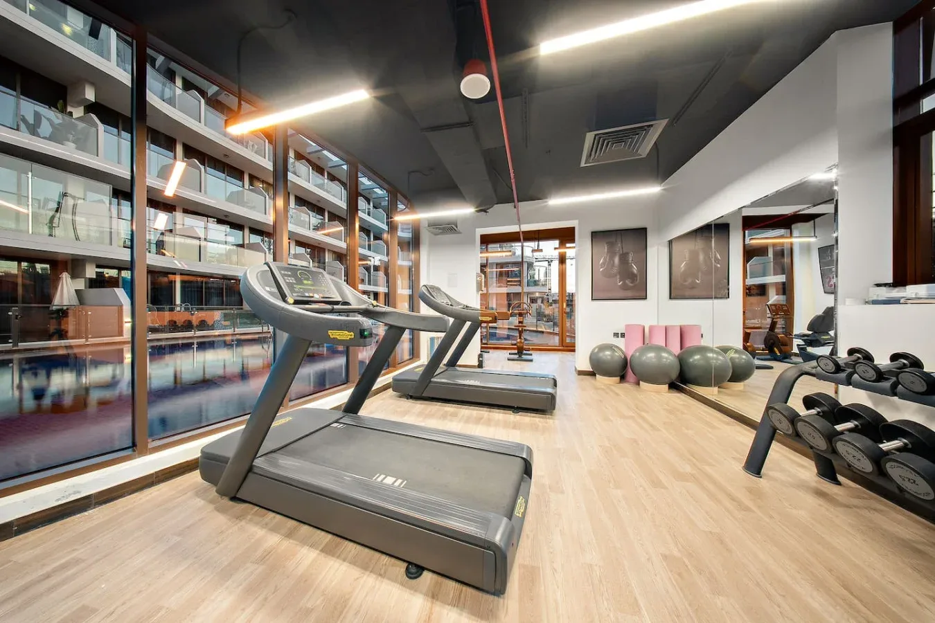 A gym with treadmills and weights on a light wood floor.