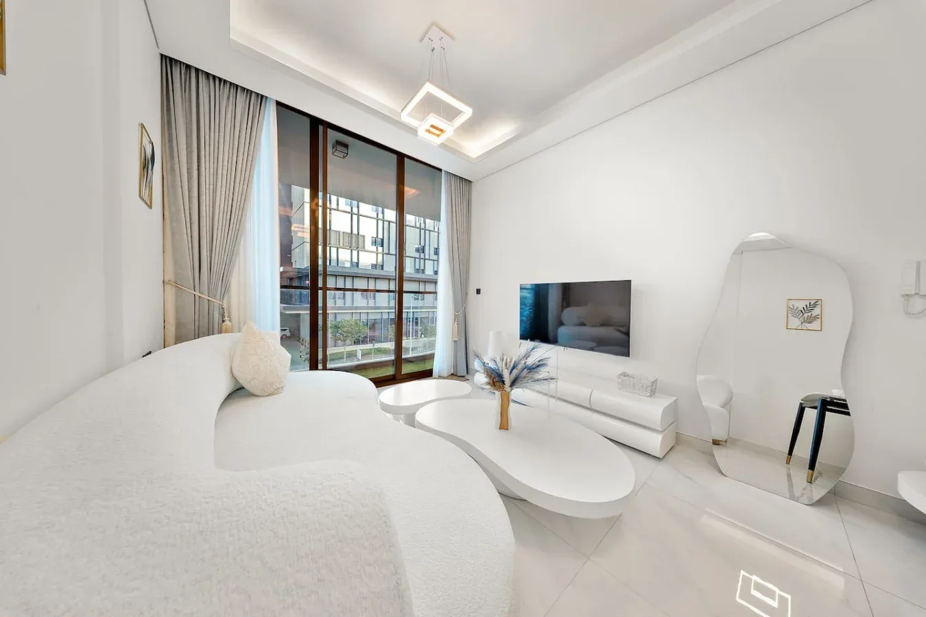 A bright living room with a white sofa, television, and tall curtained windows.