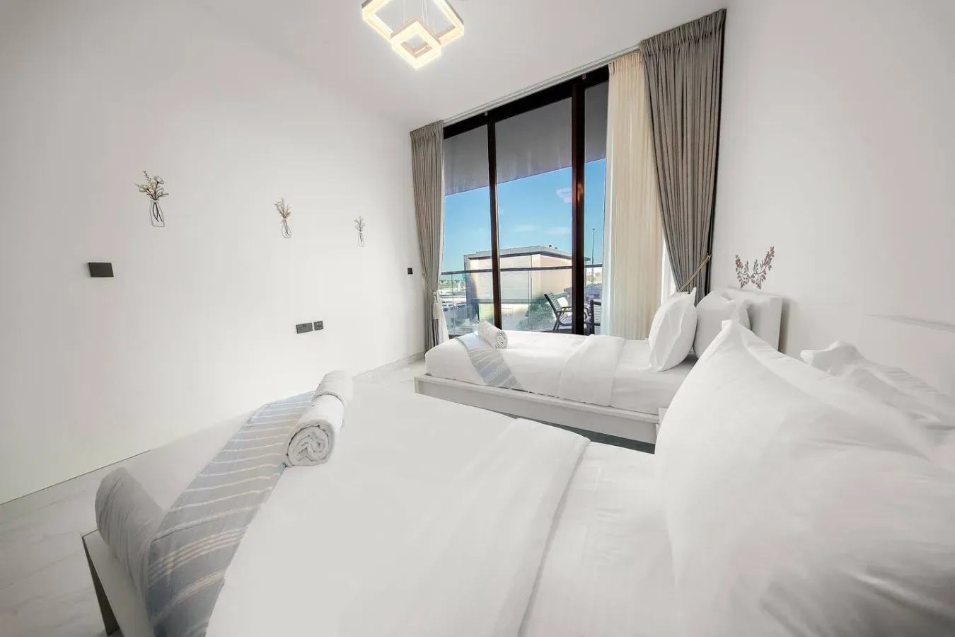 A bright bedroom with white bedding and a large window opening onto a balcony.