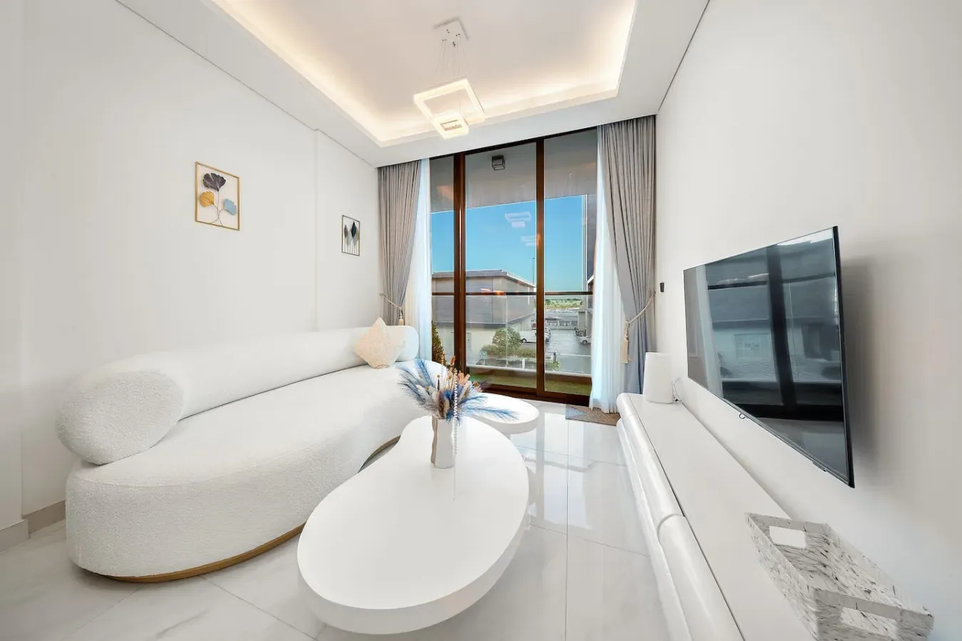 A bright living room with white seating, an oval coffee table, and a large window.