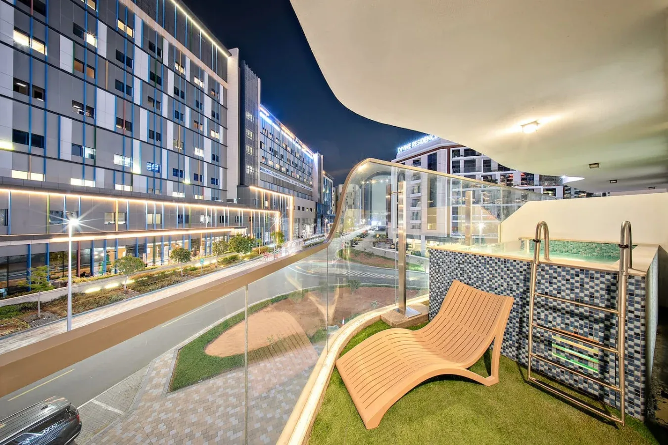 A rooftop terrace with curved lounge seating and a glass railing overlooks illuminated buildings.