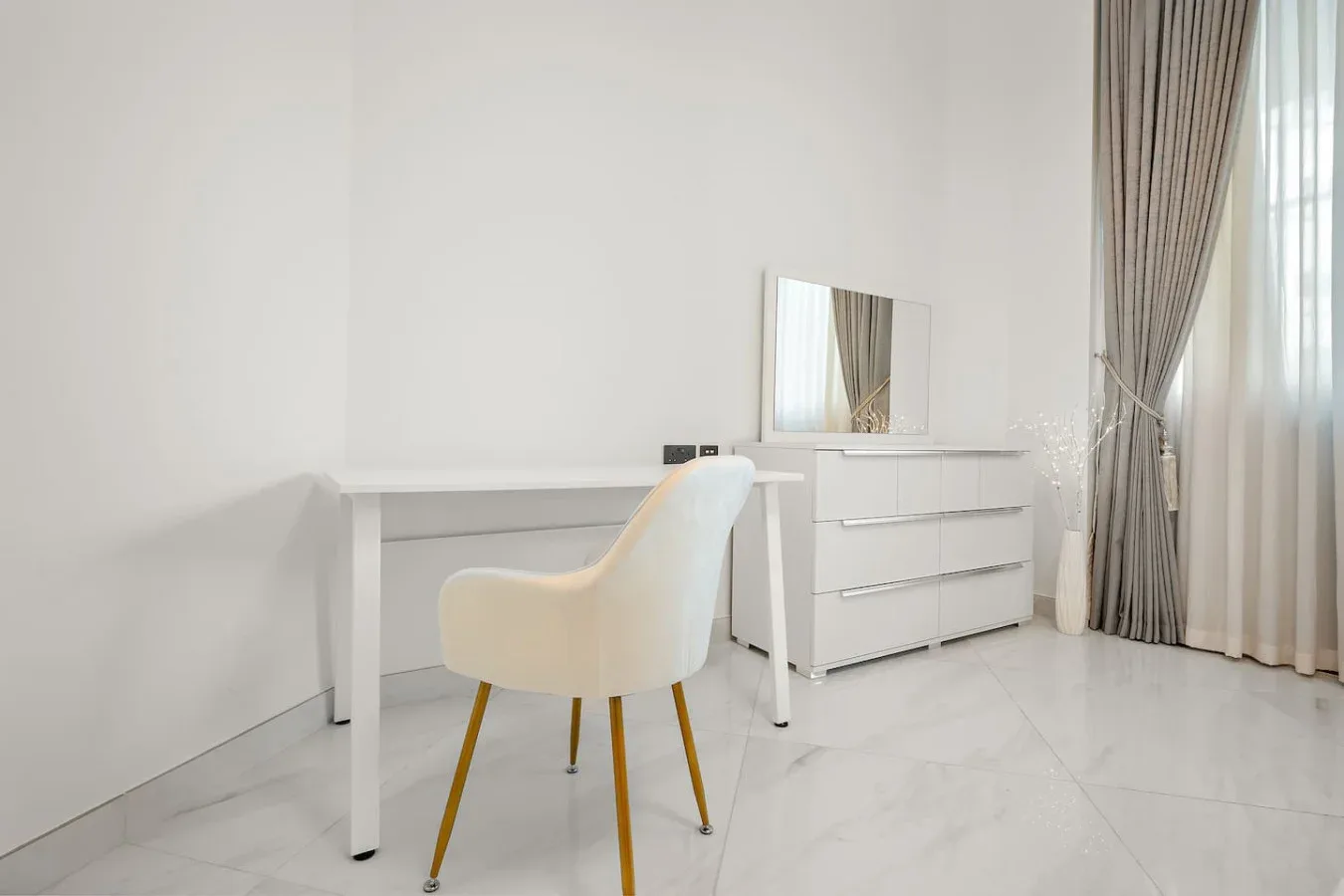 A bright room with a white desk, chair, dresser, and curtained window.