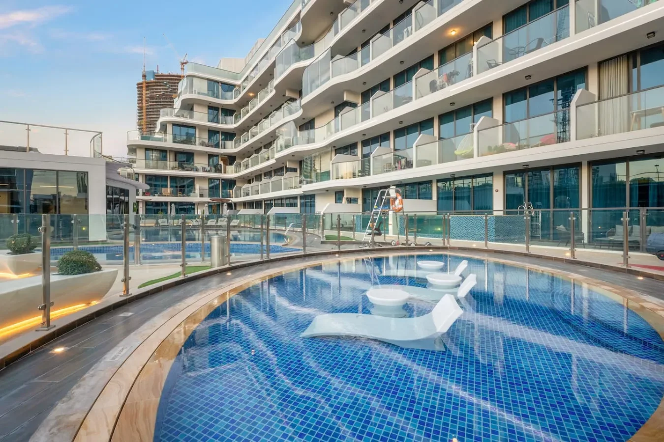 Una piscina exterior curva está junto a un edificio moderno con balcones de vidrio.