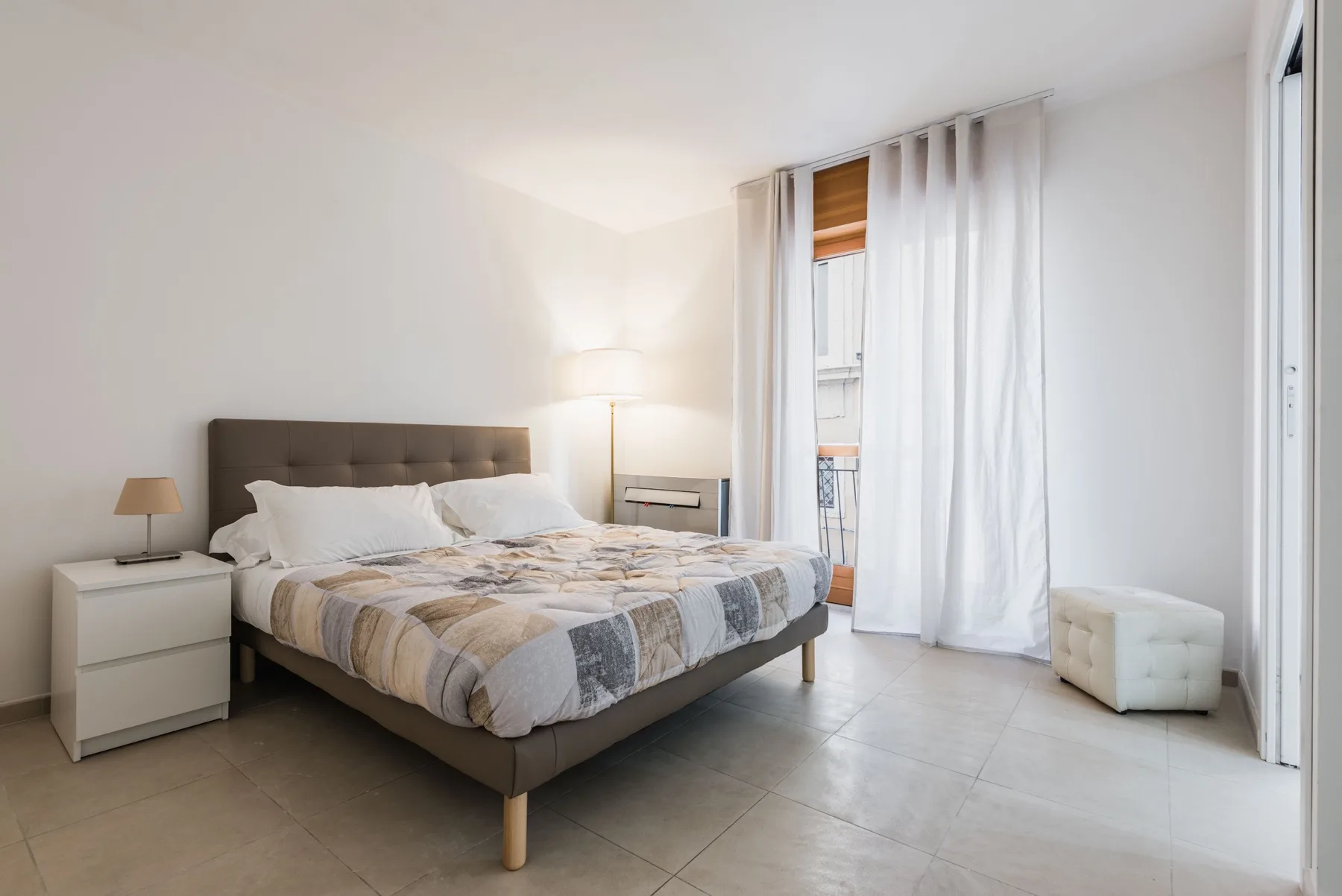 Un dormitorio luminoso con una cama grande, mesitas de noche y cortinas junto a la ventana.