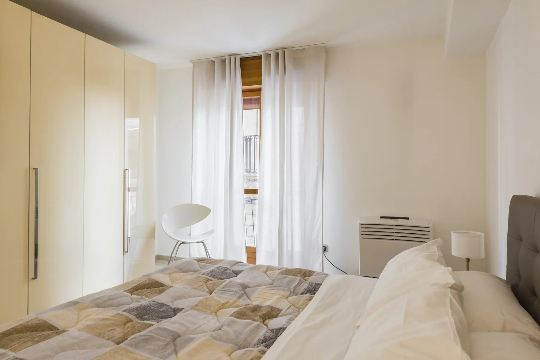Un dormitorio con una cama, armarios empotrados y cortinas translúcidas junto a la ventana.