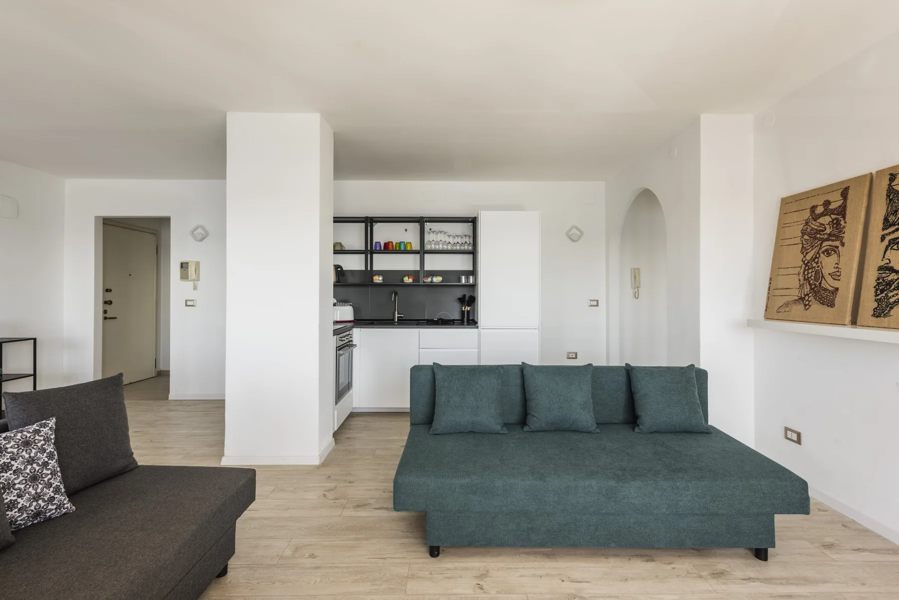 Una sala luminosa con un sofá verde azulado y una cocina abierta al fondo.