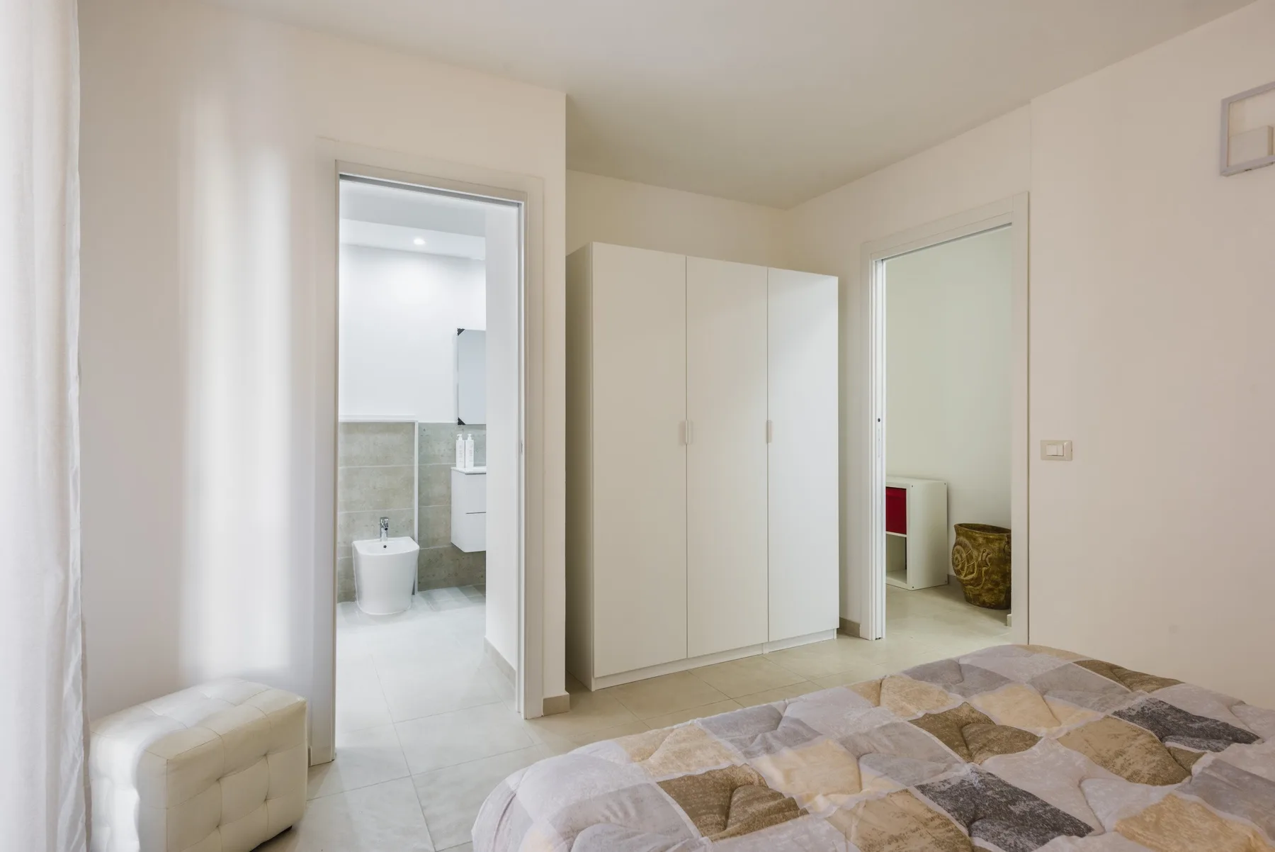 Un dormitorio con una cama, un armario blanco y una puerta abierta hacia un baño.