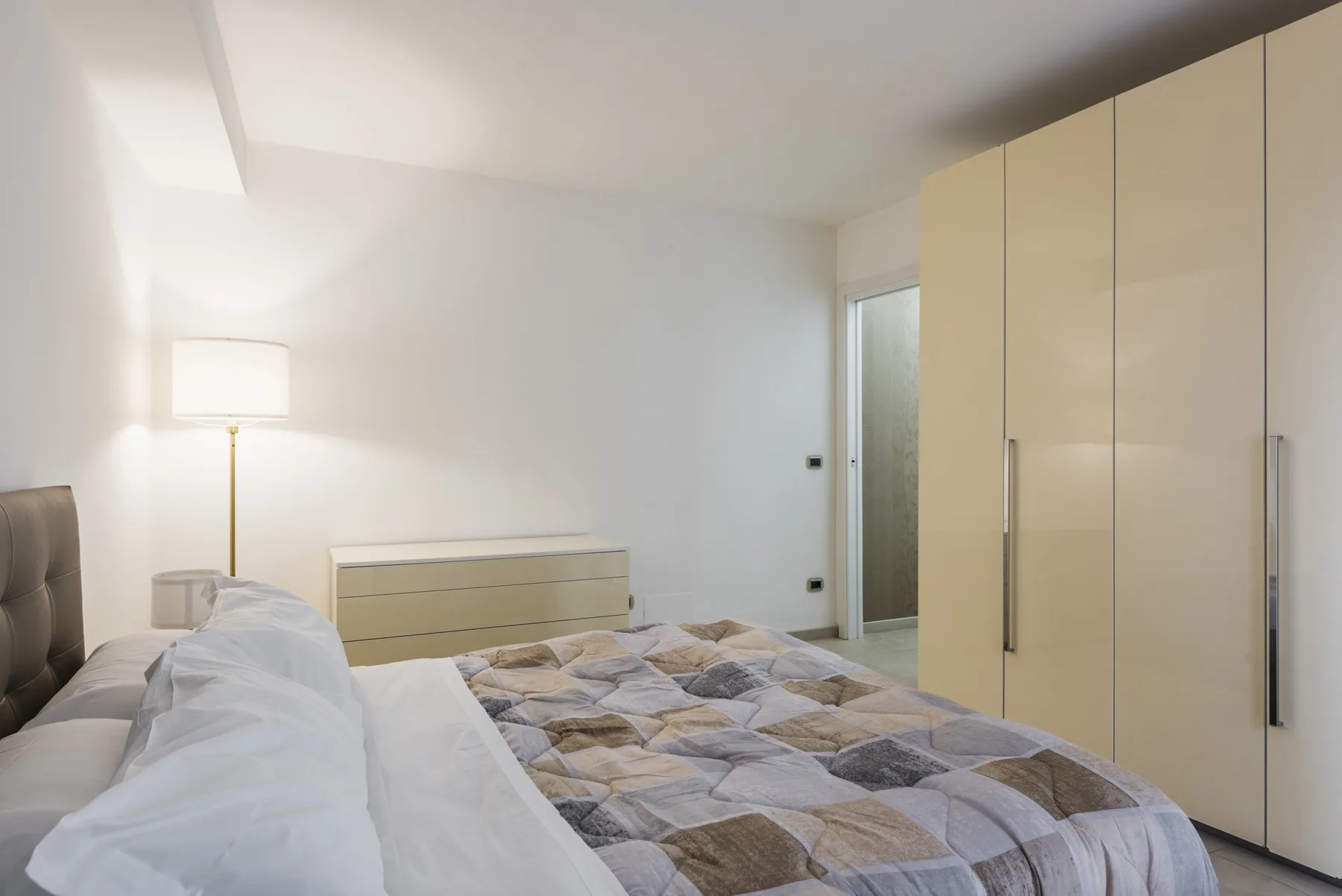 Un dormitorio con una cama, ropa de cama estampada y armarios altos.