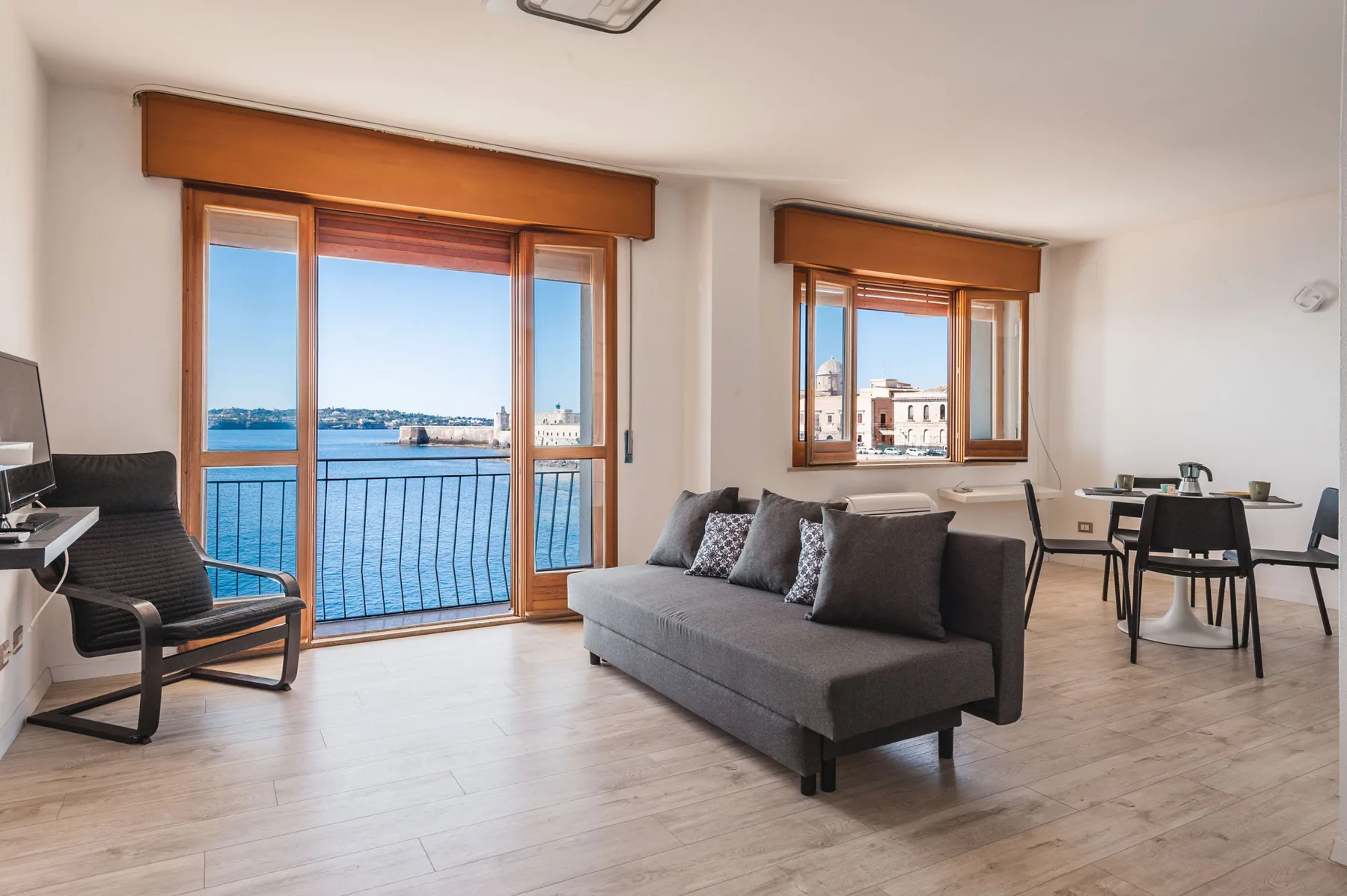 Una sala de estar y comedor con asientos junto a grandes ventanas con vistas al agua.