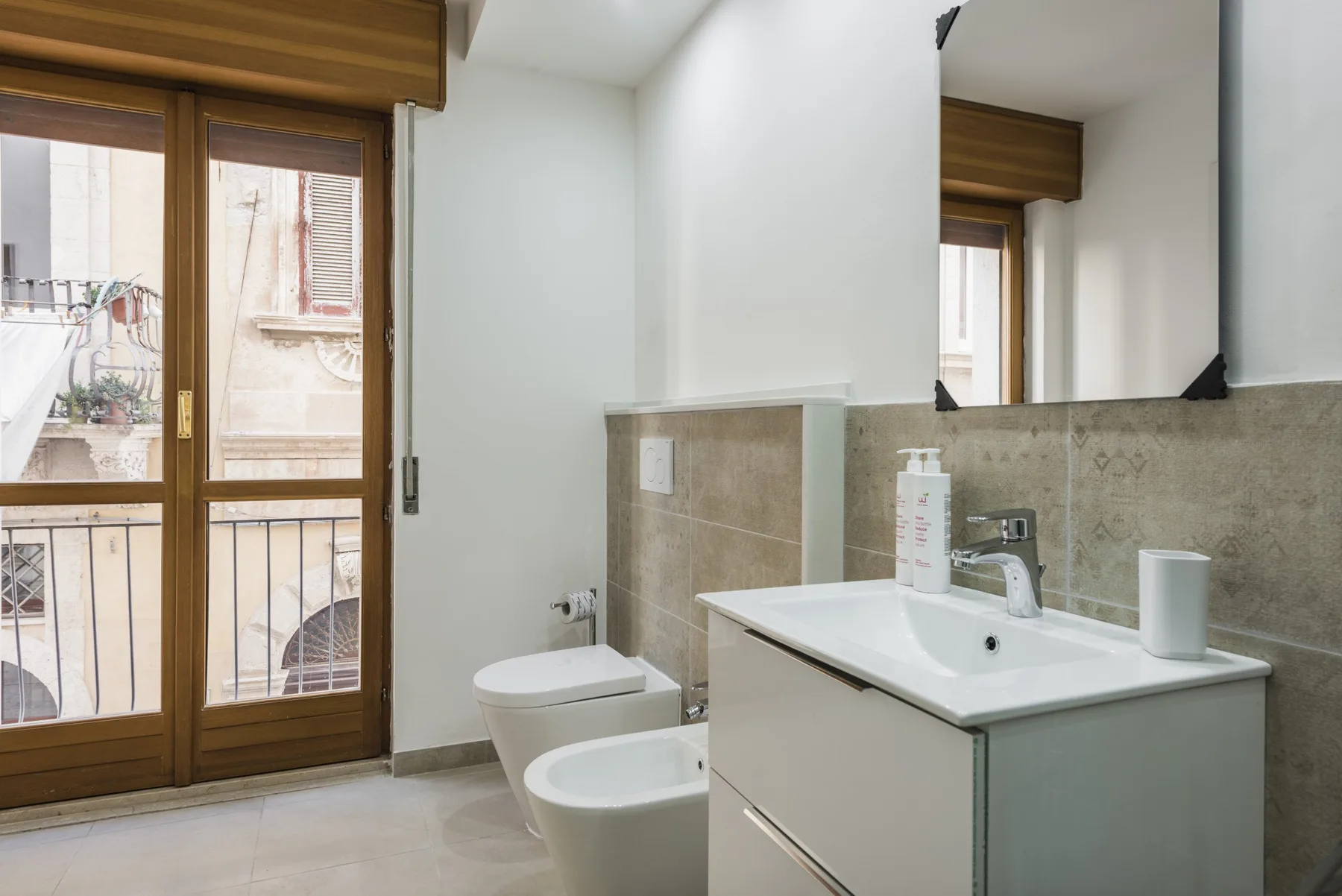 Un baño luminoso con lavabo, inodoro y puertas de vidrio que dan a un balcón.