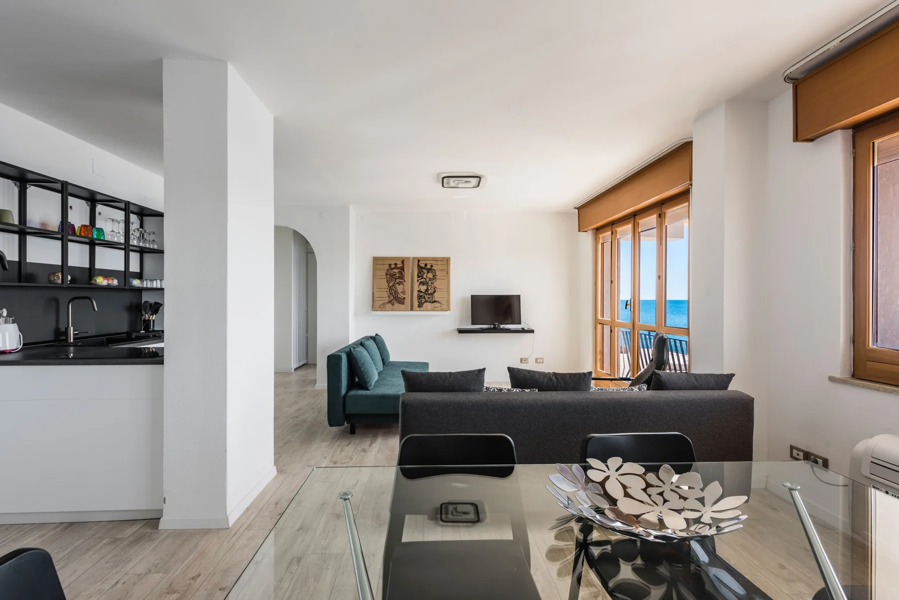 Una sala luminosa con asientos, una mesa de comedor de vidrio y ventanas grandes.