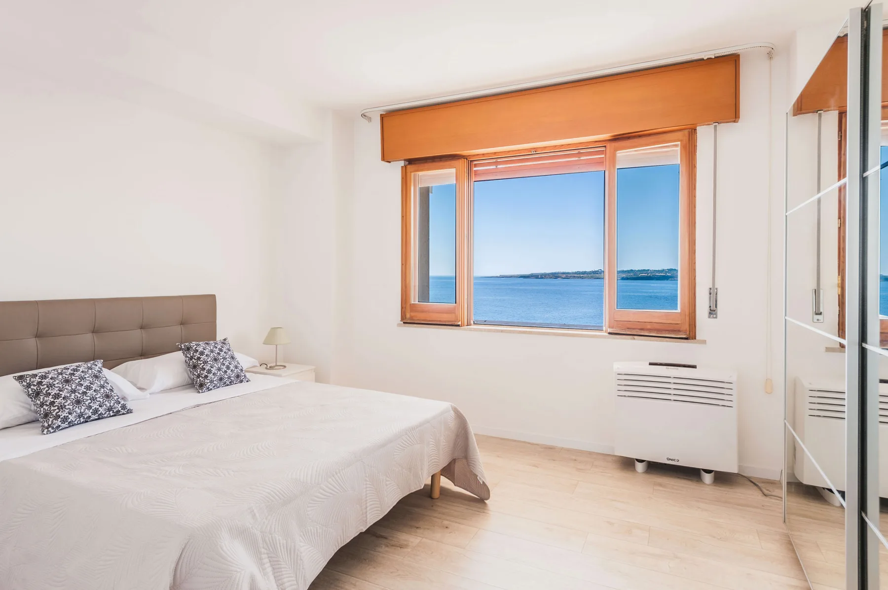 Un dormitorio luminoso con una cama junto a una ventana con vistas al mar.