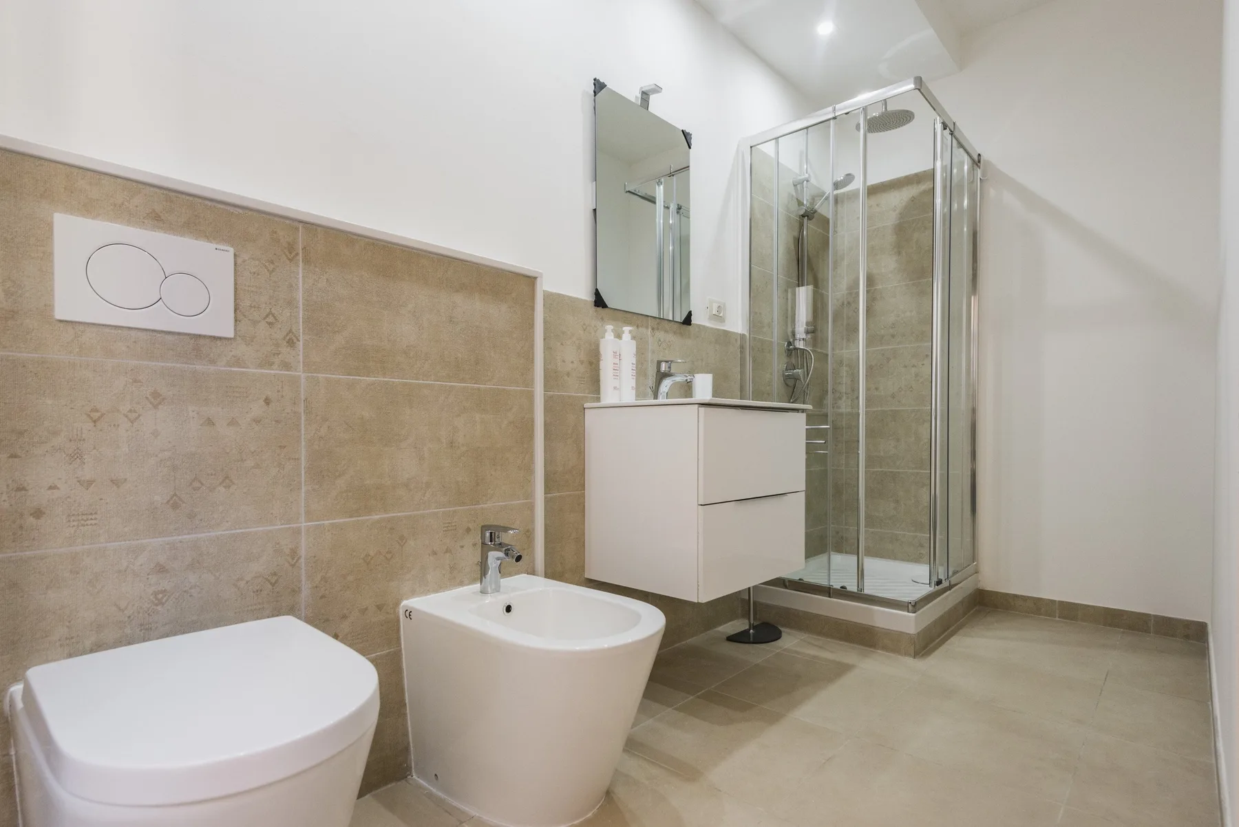Un baño con azulejos, una ducha de vidrio, un lavabo suspendido y un inodoro.
