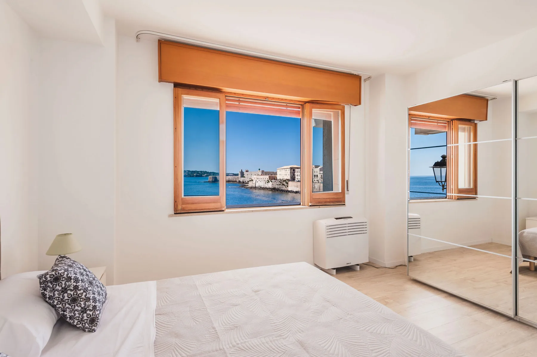 Un dormitorio con una cama junto a una ventana con vistas al paseo marítimo.
