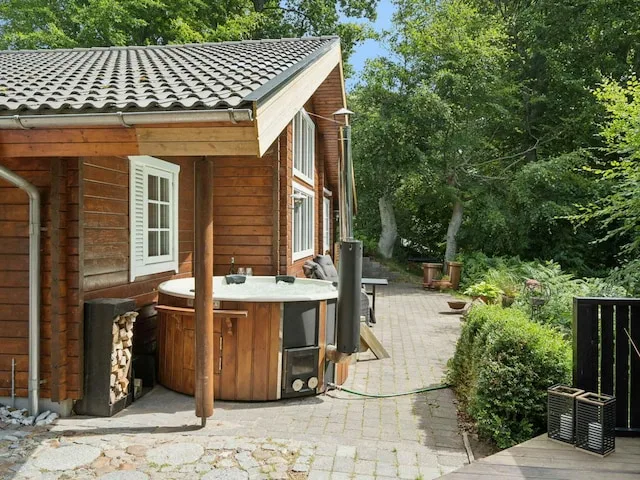 A wooden cabin opens onto a paved patio with a round outdoor hot tub.