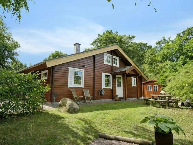 A wooden cabin stands in a leafy garden with outdoor seating.