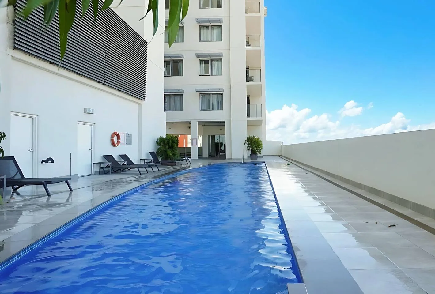 A rooftop pool beside a modern building, with lounge seating along the edge.