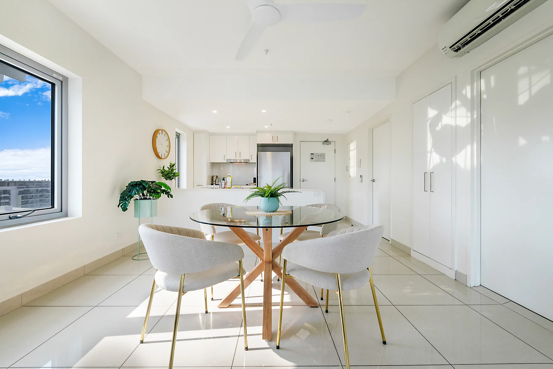 Un comedor luminoso con una mesa de vidrio, asientos y un ventilador de techo.