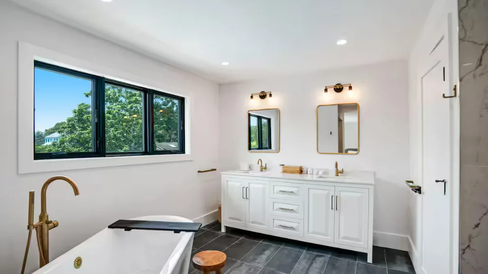 Un baño luminoso con bañera exenta, lavabo doble y una ventana grande.