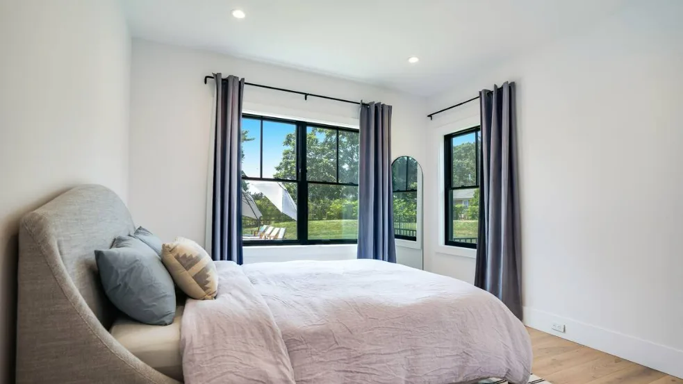 Un dormitorio luminoso con una cama junto a grandes ventanas con vistas a zonas verdes.