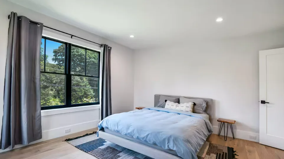 Un dormitorio con una cama junto a una ventana grande con cortinas.