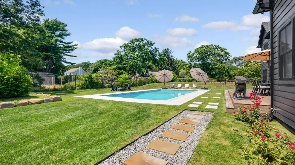 Una piscina en el patio trasero está junto al césped, un área de descanso y un sendero de piedra.