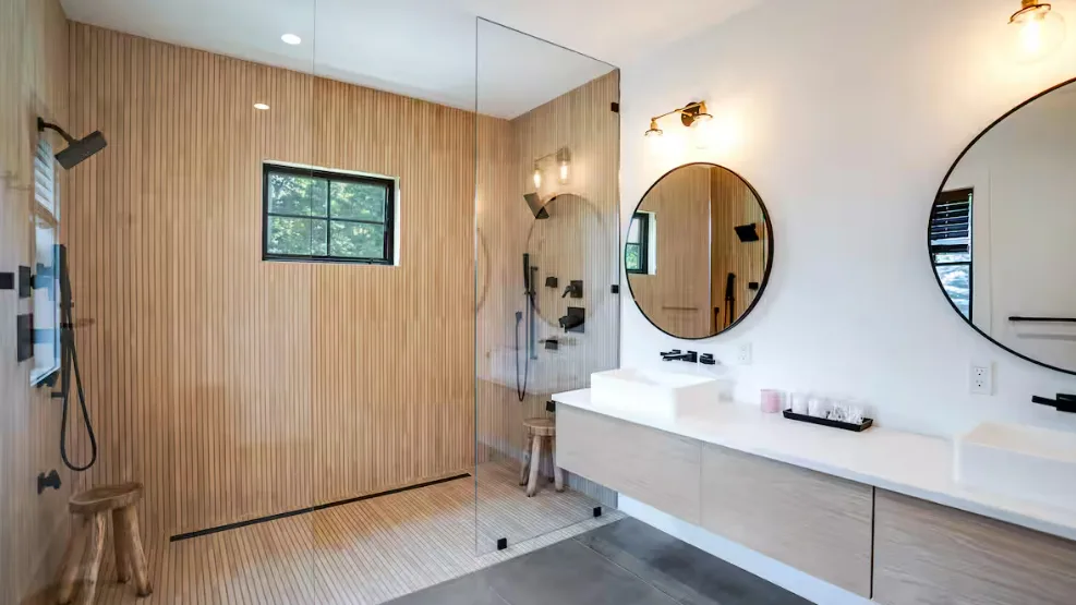 Un baño luminoso con ducha y un largo lavabo con mueble.