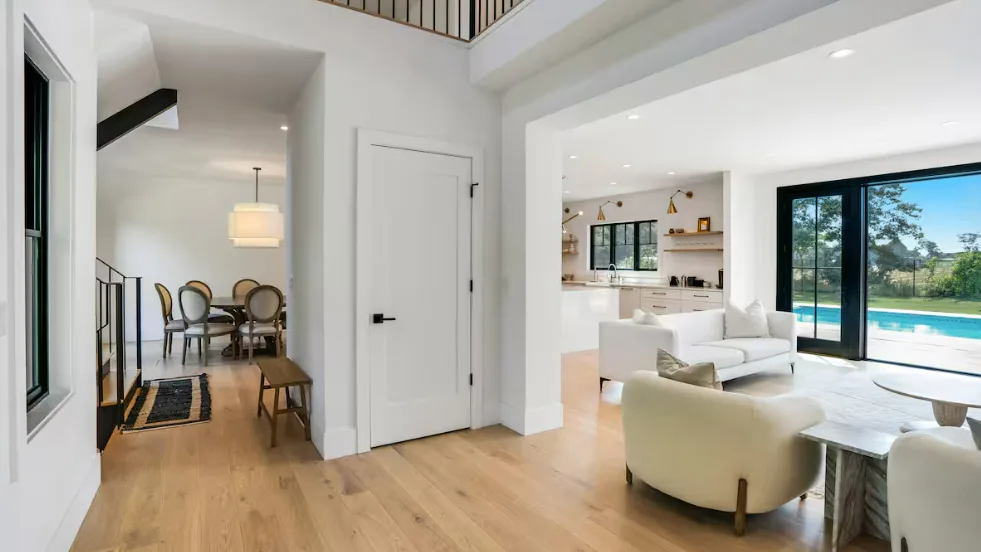 Sala de estar y cocina de concepto abierto, con asientos blancos y grandes puertas de vidrio.