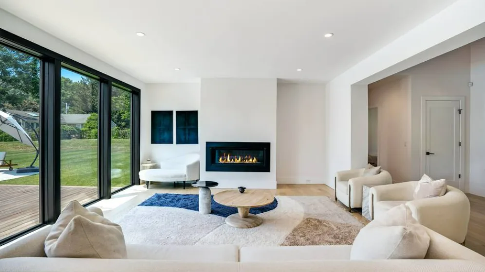 A bright living room with seating around a central fireplace and large glass doors.