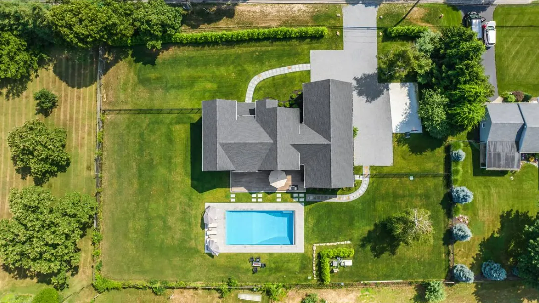 Vista aérea de una casa y una piscina rodeadas de césped y árboles.